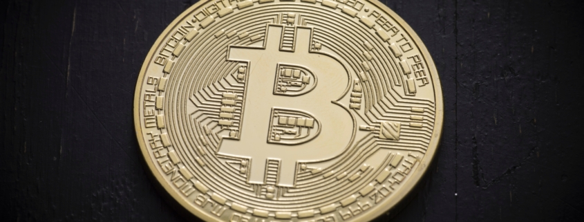 Eine goldene Bitcoin-Münze liegt auf einem dunklen Hintergrund.