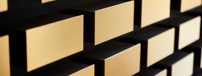 Goldene, rechteckige Blöcke ragen aus einer dunklen Wand hervor und erzeugen ein modernes, geometrisches Muster.
