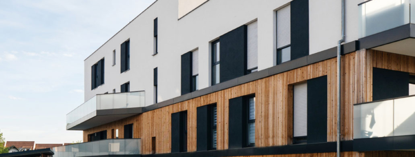 Moderne Wohnanlage mit Holz- und Glaselementen, mehreren Balkonen und großen Fenstern.