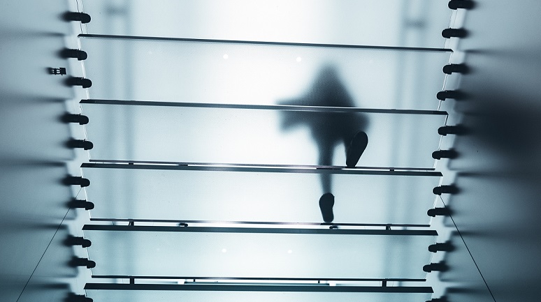 Eine Person geht eine transparente Treppe hinauf, von unten fotografiert, sodass nur die Silhouette sichtbar ist.