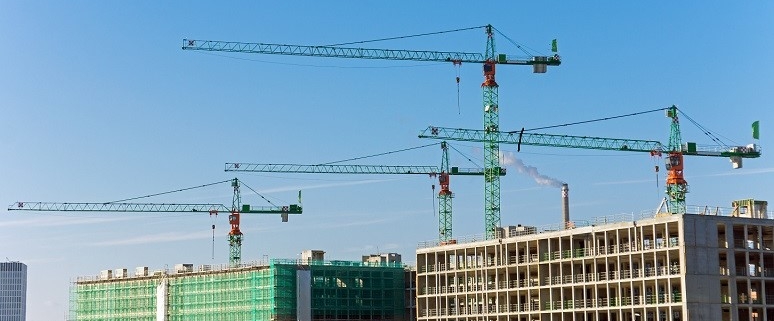 Baustelle in Berlin mit mehreren Baukränen und teilweise errichteten Gebäuden unter blauem Himmel.