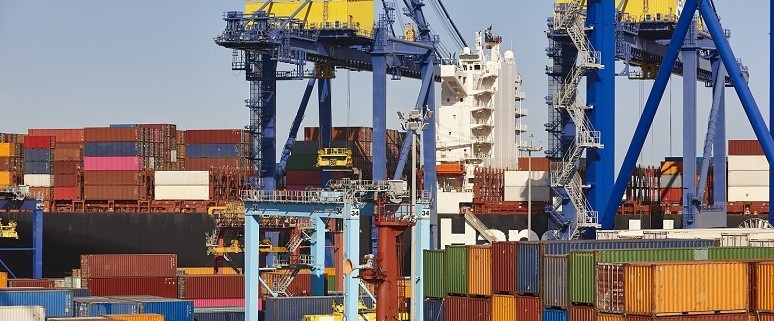 Containerschiff im Hafen mit bunten Frachtcontainern und großen blauen Kränen.