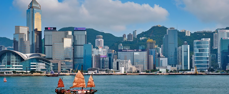 Skyline von Hongkong mit traditionellem Segelboot im Vordergrund und modernen Wolkenkratzern im Hintergrund.