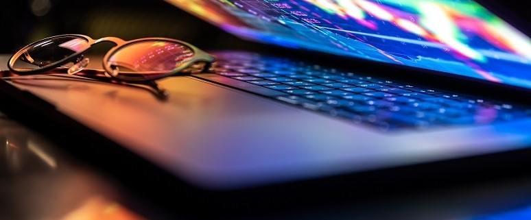 Laptop mit bunter Finanzgrafik auf dem Bildschirm und einer Brille auf der Tastatur.