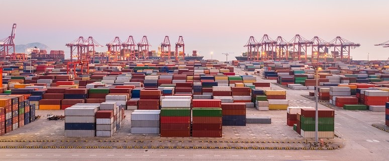 Hafen mit zahlreichen Containern und Kränen bei Sonnenuntergang.