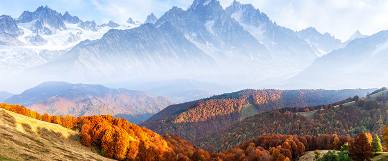 Das Bild zeigt einen Weitblick in ein bewaldetes Tal mit herbstlichen Tönen und einem mit Bergpanorama im Hintergrund.