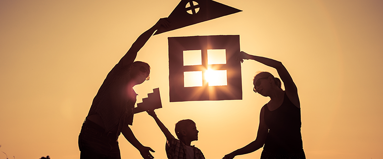 Eine Familie hält ausgeschnittene Formen eines Hauses und Fensters in die Luft, durch die die Sonne scheint.