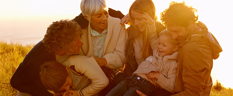Eine fröhliche Familie sitzt im Freien auf einer Wiese im Sonnenuntergang.