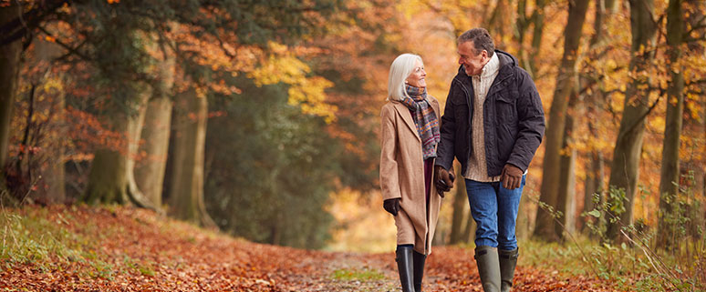 Älteres Paar lächelt sich an und geht in einem herbstlichen Wald spazieren