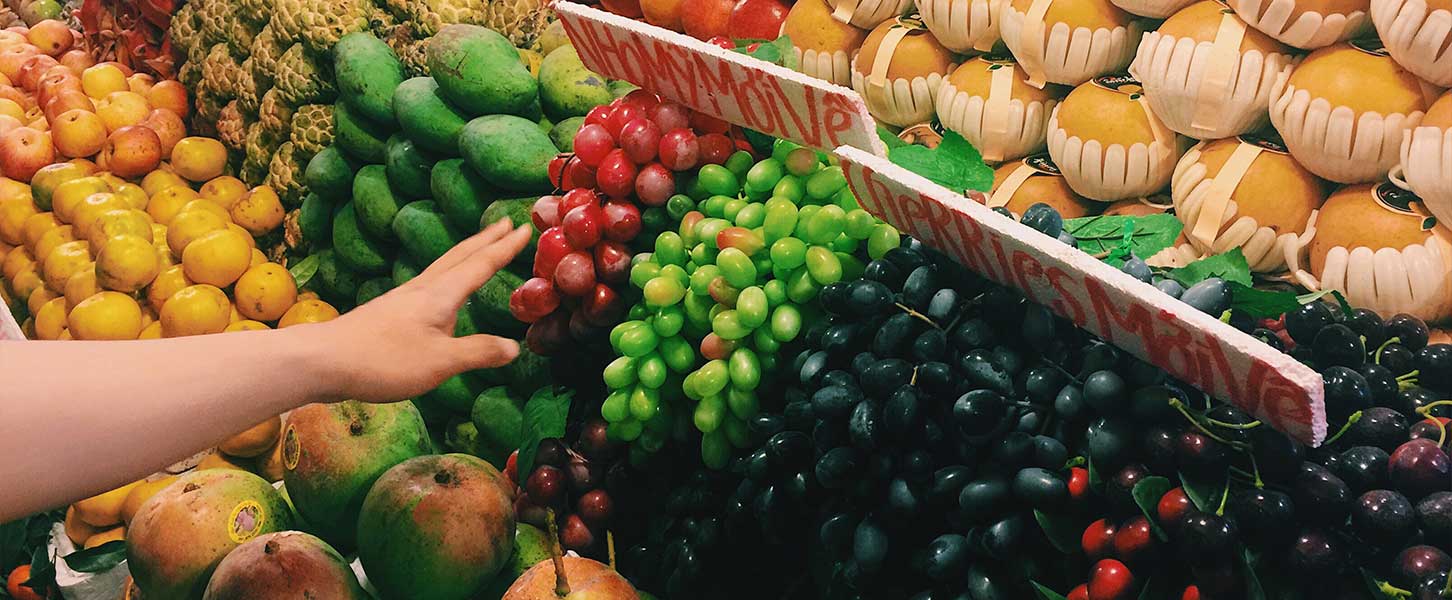 Nahaufnahme eines Marktstands mit verschiedenen Obstsorten in Reihen und einer Hand, die Trauben greift