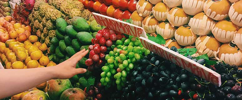 Nahaufnahme eines Marktstands mit verschiedenen Obstsorten in Reihen und einer Hand, die Trauben greift