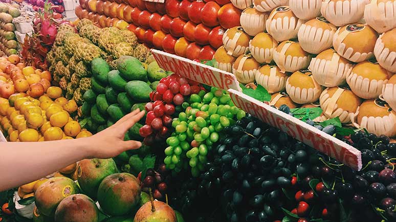 Nahaufnahme eines Marktstands mit verschiedenen Obstsorten in Reihen und einer Hand, die Trauben greift
