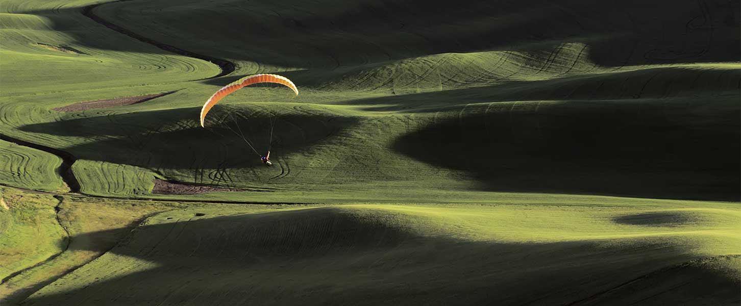 Paraglider über hügeliger Landschaft mit wechselnden Licht- und Schattenflächen