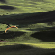 Paraglider über hügeliger Landschaft mit wechselnden Licht- und Schattenflächen