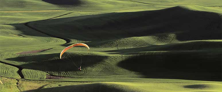 Paraglider über hügeliger Landschaft mit wechselnden Licht- und Schattenflächen