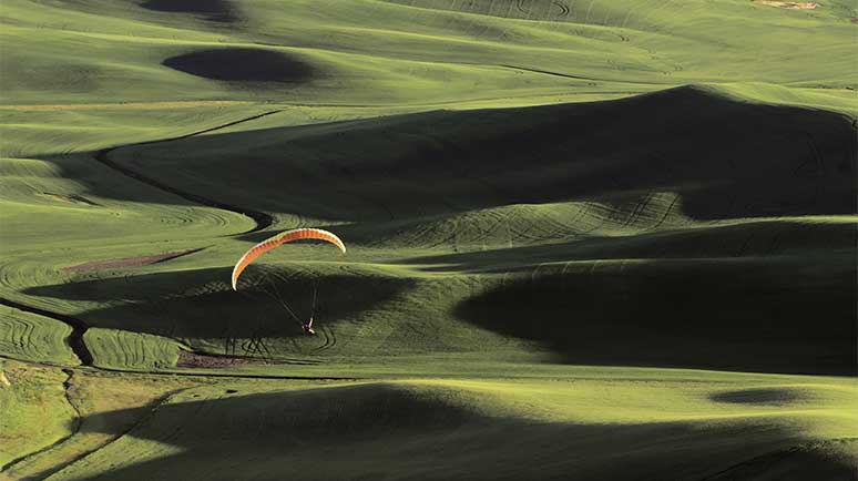 Paraglider über hügeliger Landschaft mit wechselnden Licht- und Schattenflächen