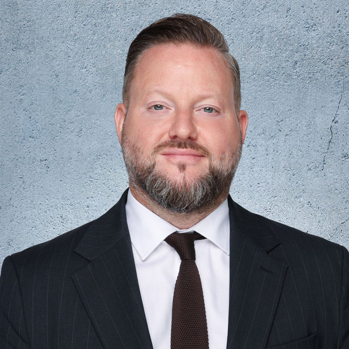 Auf dem Bild ist Dennis-Manuel Peters zu sehen, der einen dunklen Anzug und ein weißes Hemd trägt