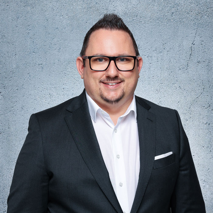 Auf dem Bild sieht man Florian Winklhofer mit einem dunklen Anzug und weißem Hemd