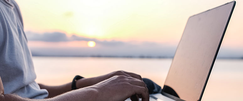 Auf dem Bild sieht man wie eine Person vor einem See an einem Laptop arbeitet