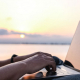 Auf dem Bild sieht man wie eine Person vor einem See an einem Laptop arbeitet