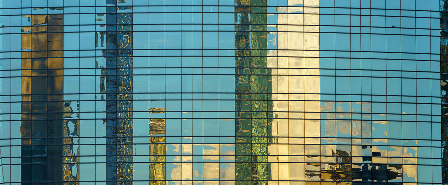 Glasfassade eines Hochhauses mit Spiegelung der Skyline verschiedener Wolkenkratzer