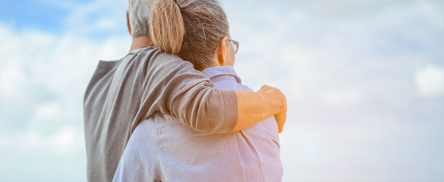 A senior couples embrace the beach in the morning, look at the bright blue skies and plan life insurance with a happy retirement concept.