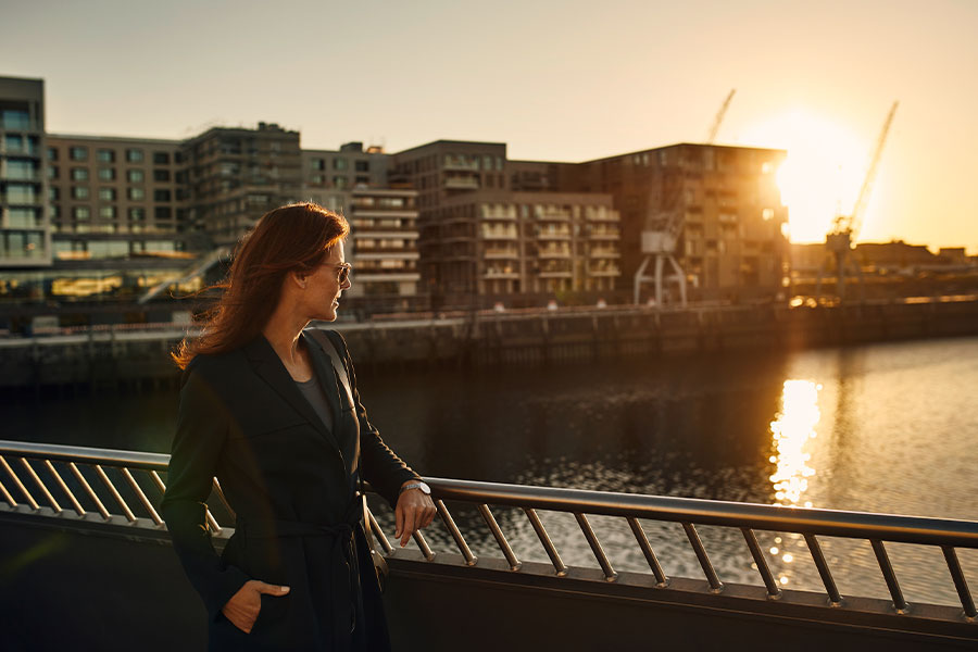 Eine Frau schaut auf die Elbe in Hamburg. Im Hintergrund sieht man Mehrfamilienhäuser und den Sonnenuntergang